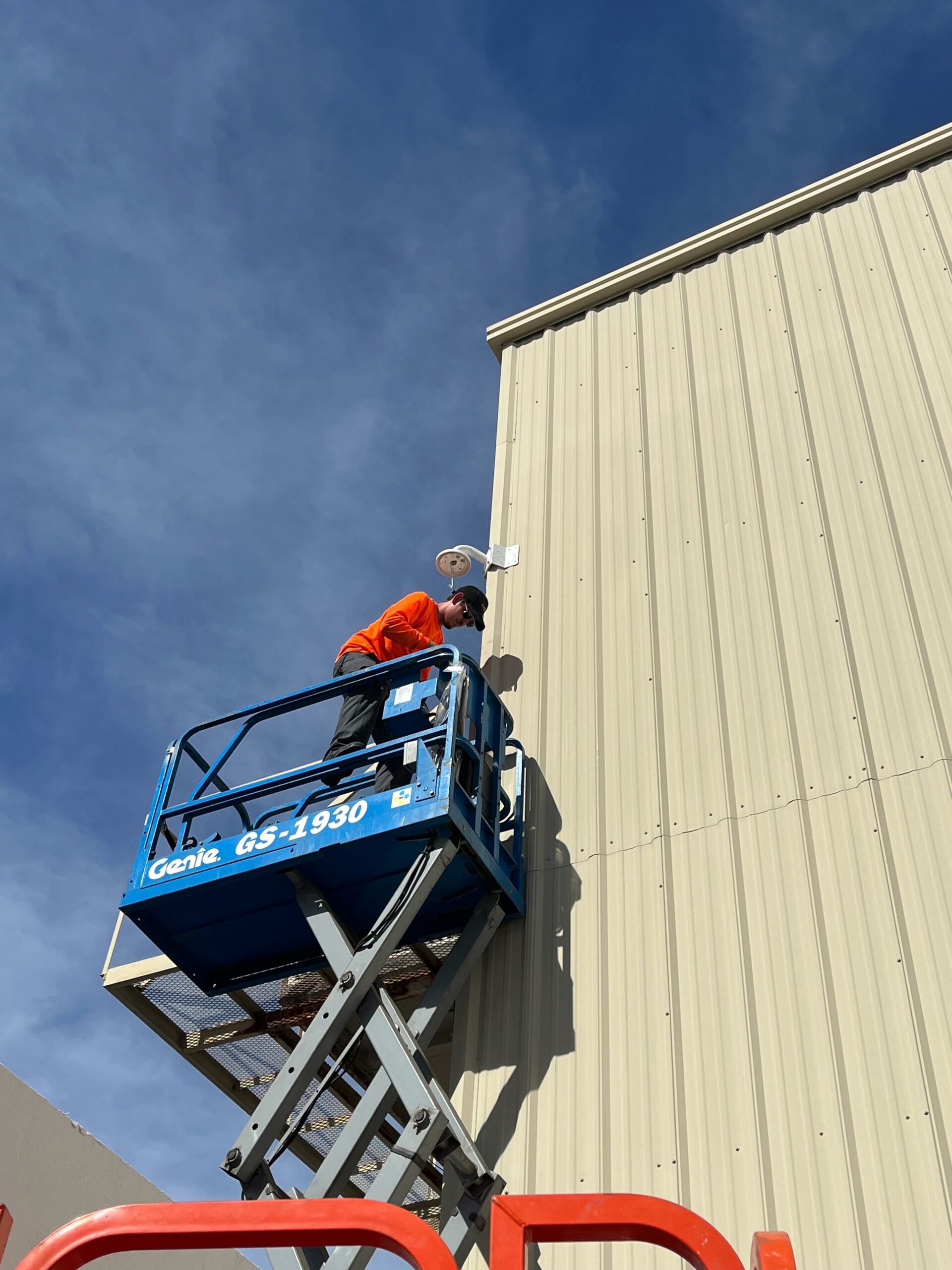 Phoenix Security technician installing a security camera on a commercial building from a scissor lift